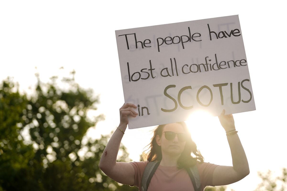 A woman holds a sign that says, "The people have lost all confidence in SCOTUS."
