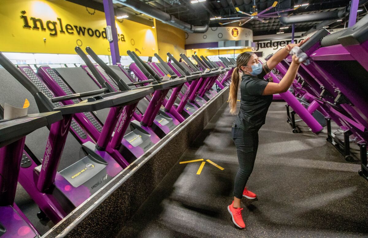 A woman wipes down treadmills indoors.