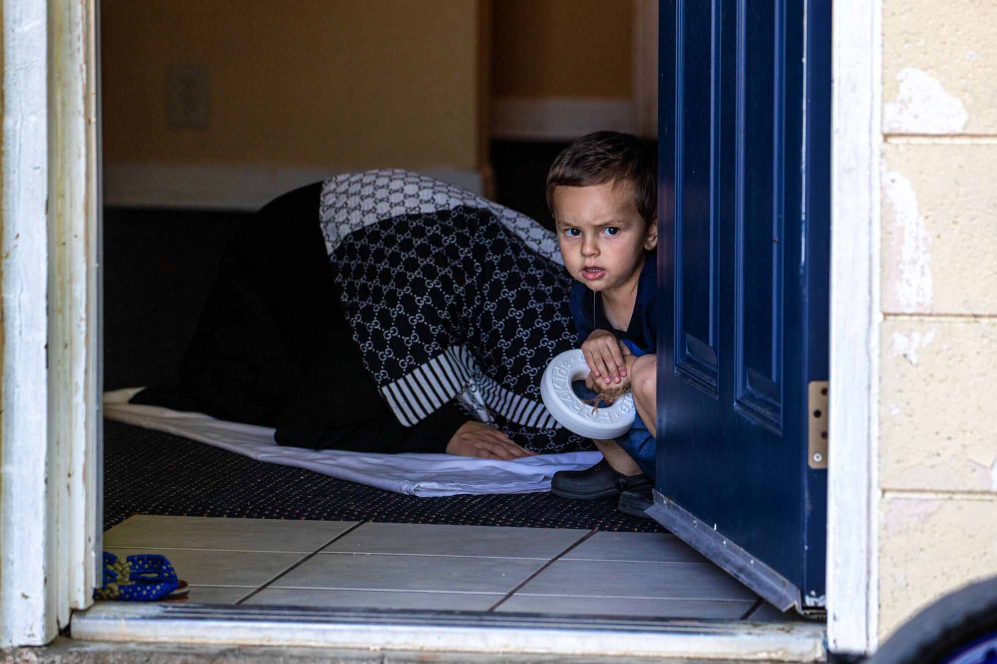 A child looks out the door as an Afghani woman  offers prayers in her room 