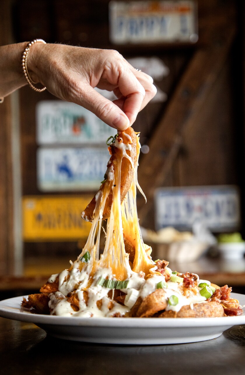A hand lifts cheesy strings from a plate of cheese fries.