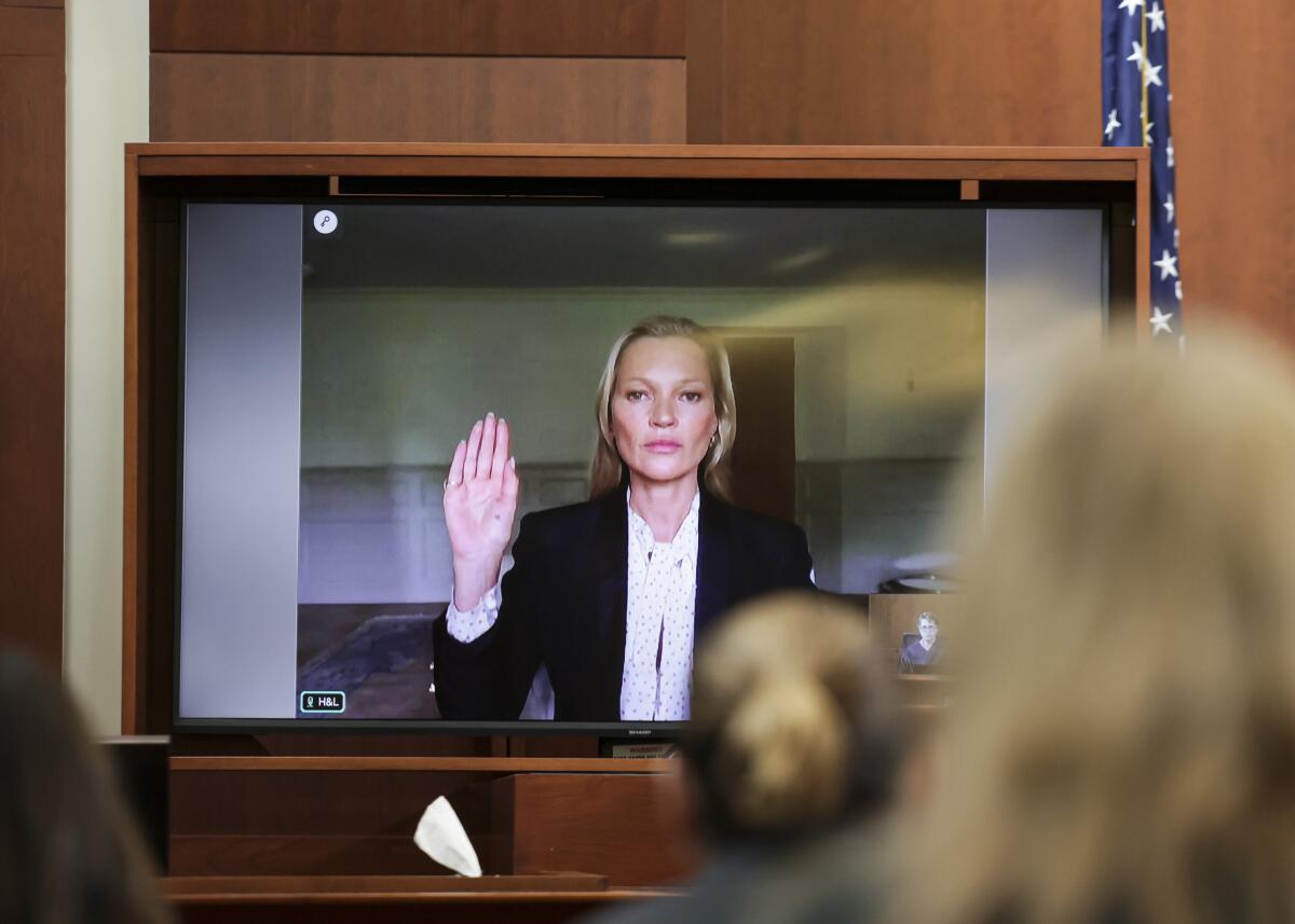 A woman in a black suit raising a hand on a screen in a courtroom.