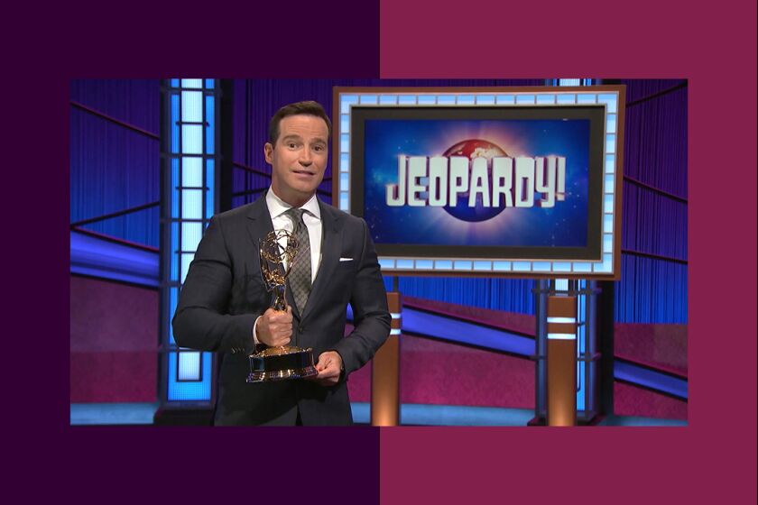 a man stands holding an Emmy statue on the set of Jeopardy
