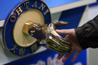 A hand reaches to shake a golden-colored replica of a hand, in a round plaque that reads "Ohtani’" in English and Japanese.