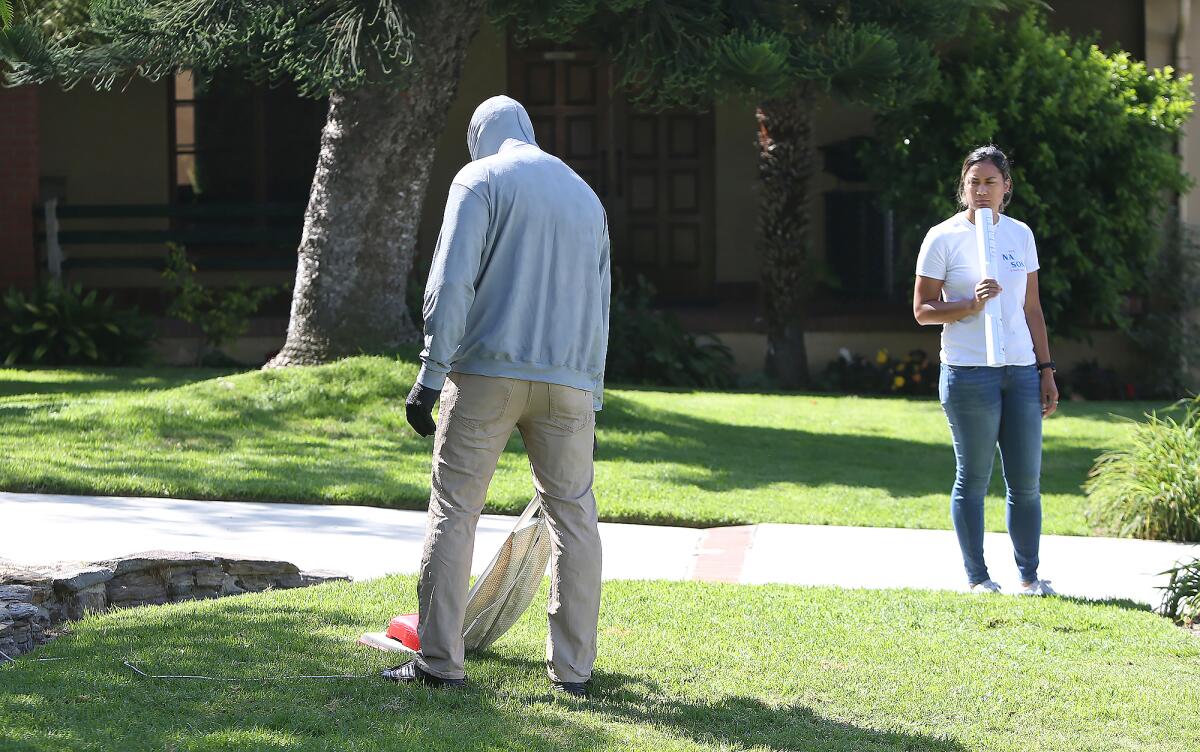 A hooded figure vacuuming the grass gets the attention of a passerby in front of Laguna Beach City Hall. It's part of a temporary public sculpture installation by artist Mark Jenkins.