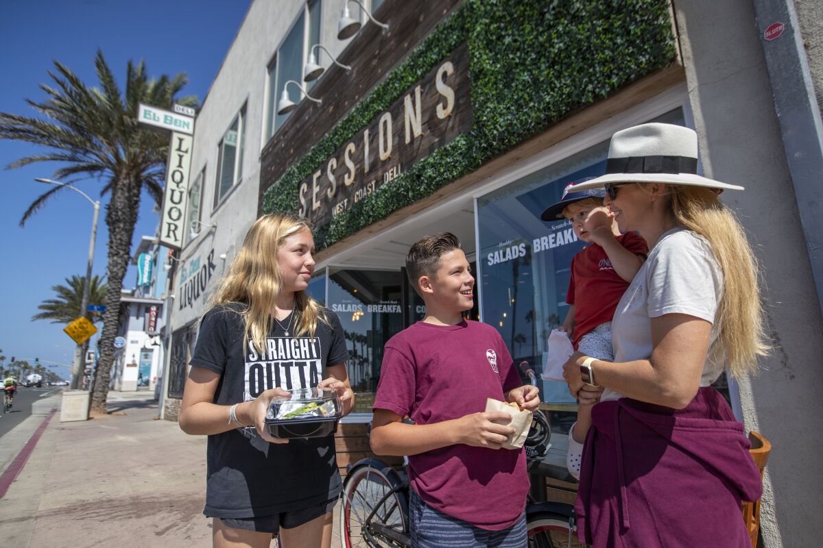 A family holds to-go containers outside Sessions West Coast Deli.