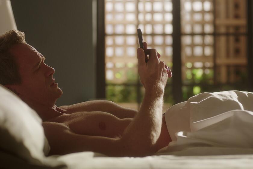A shirtless man laying in bed looking at his phone