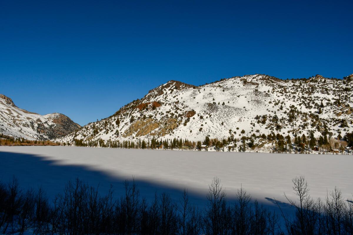 Um lago congelado visto com árvores e montanhas cobertas de neve ao redor.