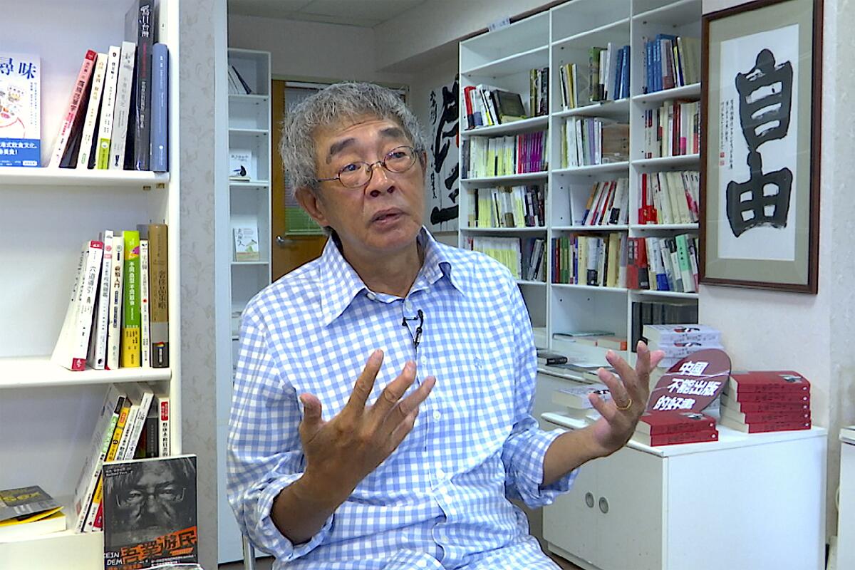 A man gestures while talking amid shelves lined with books.