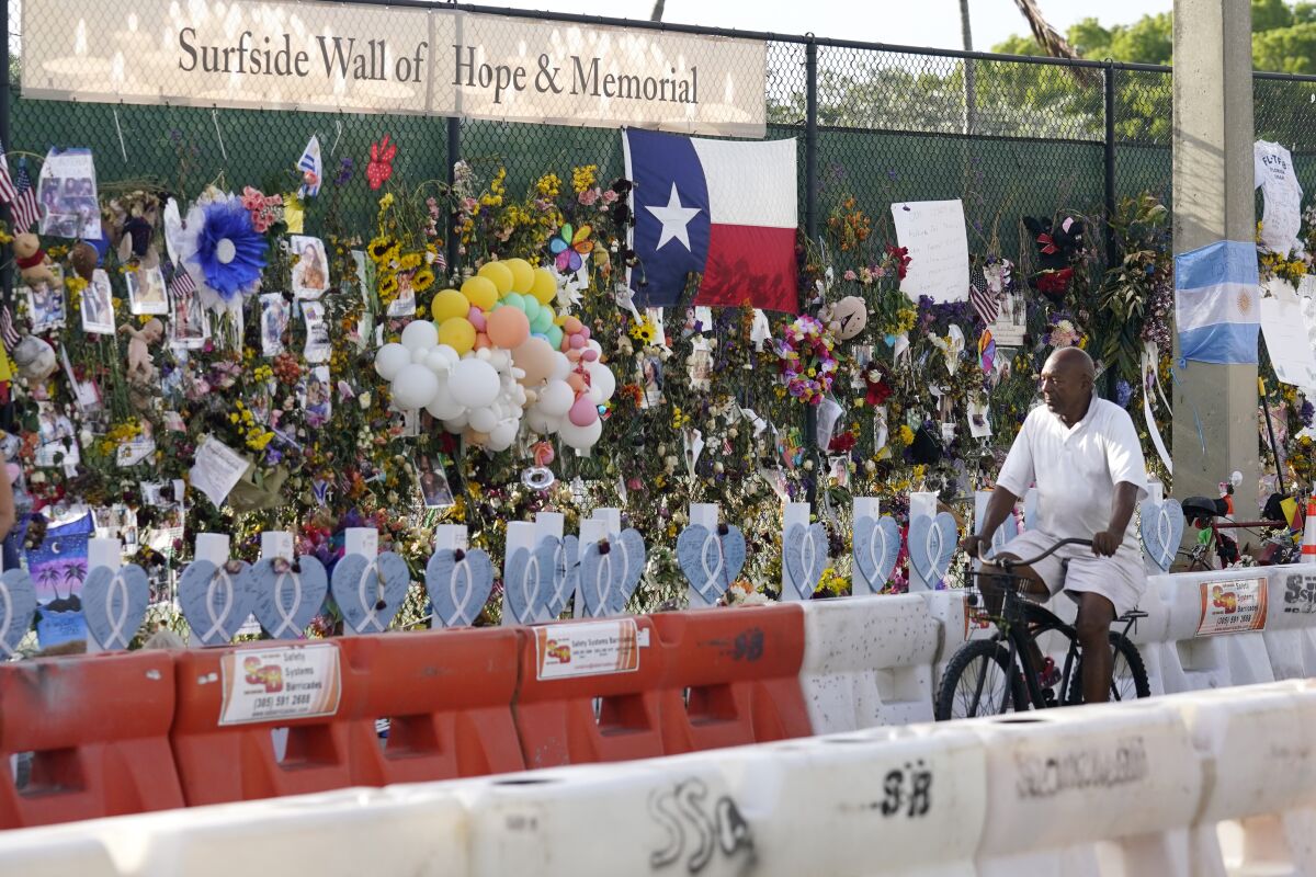 A cyclist rides past a makeshift memorial recognizing the victims of the partially collapsed Champlain Towers South building, as removal and recovery work continues at the site, Tuesday, July 13, 2021, in Surfside, Fla. (AP Photo/Lynne Sladky)