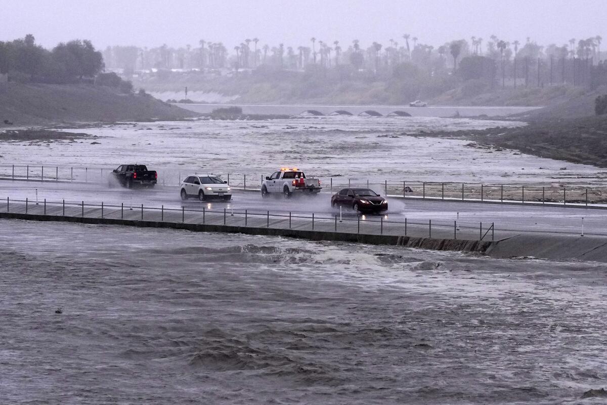 Vehicles cross a flood-control basin that has almost reached the street in Palm Desert, Calif.