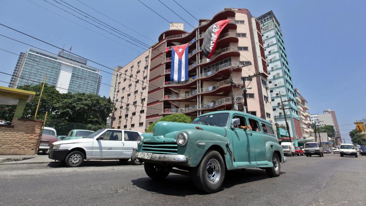 Un auto pasa frente a un edificio donde se expone la bandera cubana y la del movimiento del 26, en La Habana (Cuba).