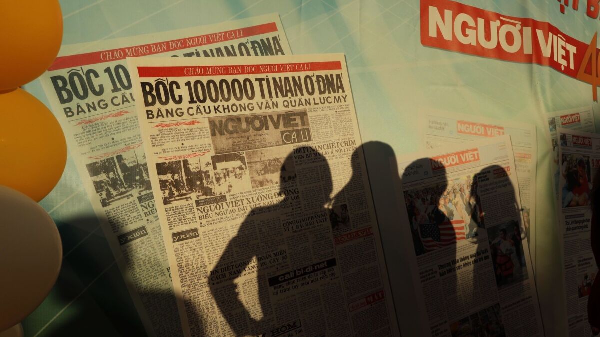 Shadows of community members are cast against a banner featuring the first edition of Nguoi Viet Daily News during a celebration of the newspaper’s 40th anniversary in Westminster.