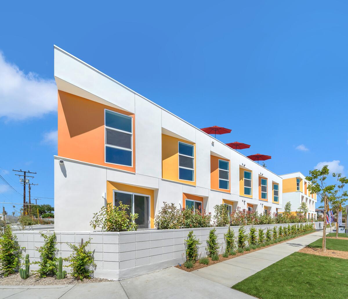 A two-story apartment complex by DE Architects features orange and yellow trim around the windows and a roof deck.