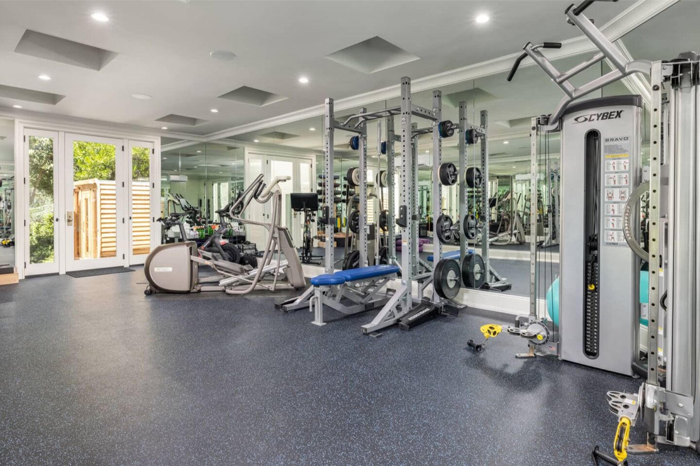 The gym has equipment and windows overlooking greenery.
