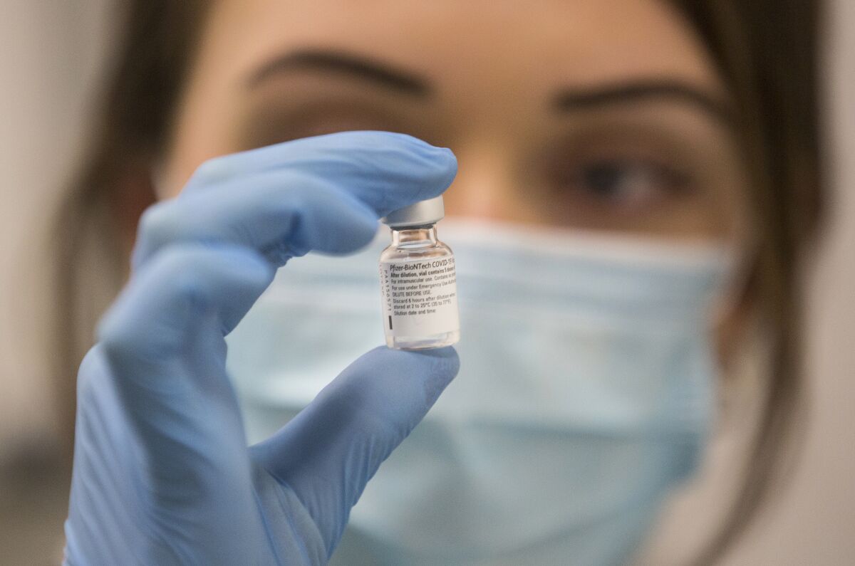 A worker holds a vial of the Pfizer-BioNTech COVID-19 vaccine in front of her face