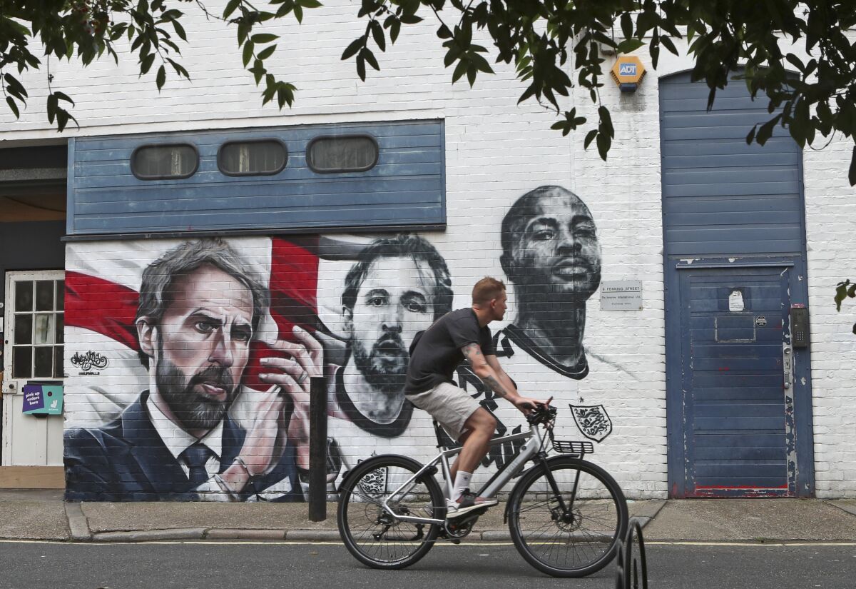A man cycles past a mural depicting England's manager Gareth Southgate, captain Harry Kane and Raheem Sterling, from left, painted on a wall near Vinegar Yard in south London, Wednesday July 14, 2021. England lost the Euro 2020 soccer championship final match to Italy on Sunday July 11. (AP Photo/Tony Hicks)