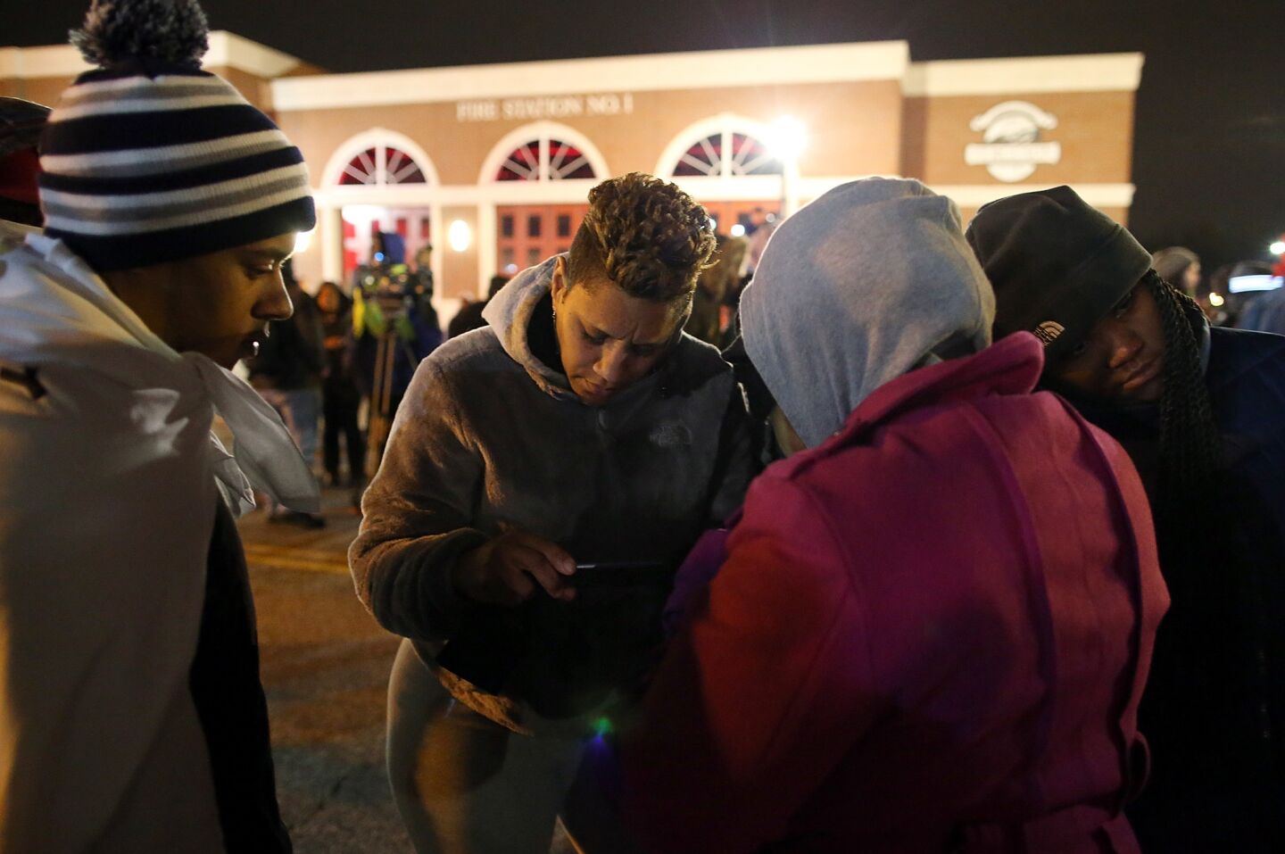 Demonstrators listen to a radio as a grand jury's decision is delivered in front of the Ferguson Police Department.