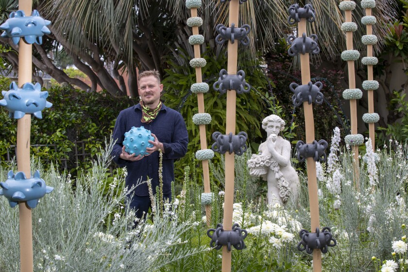 A man standing in a grassy sculpture garden holding a spheroid piece of art.