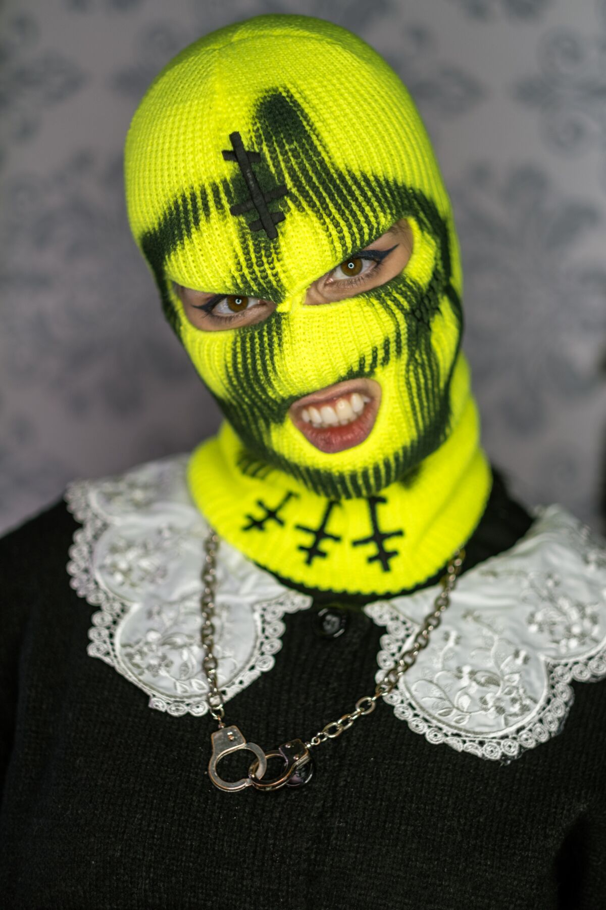 A woman sneers through a neon-colored balaclava mask.