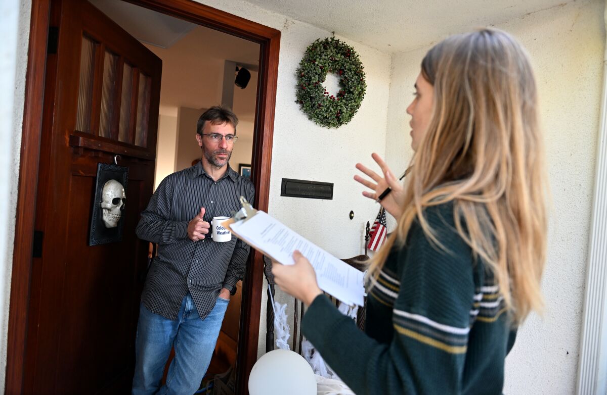 A high school senior with a clipboard talks to a man in the front doorway of his home