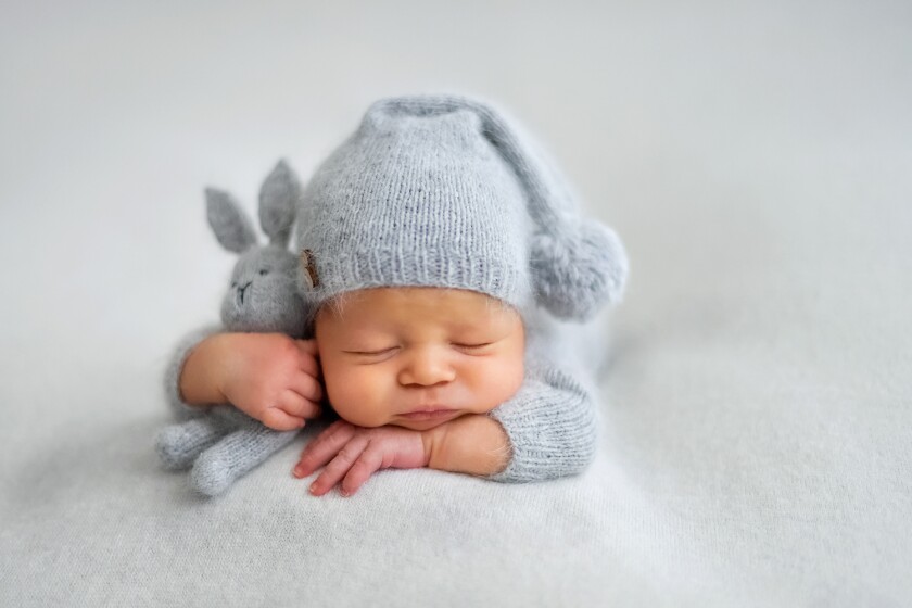 Sleeping infant in blue knitted hat holding blue-knitted stuffed bunny