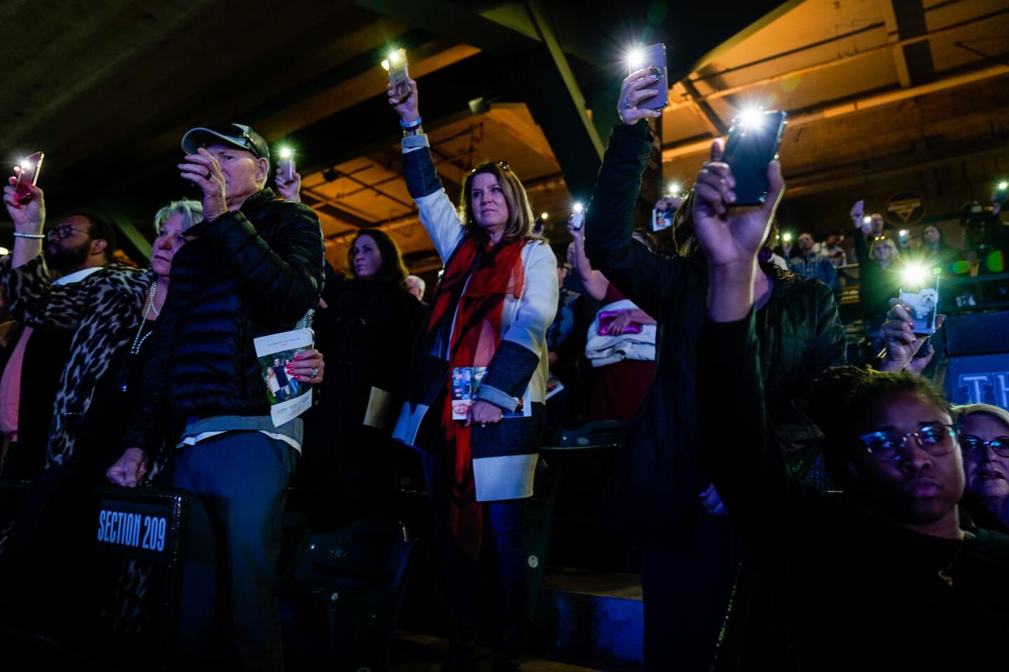 People hold up cell phones with lights on, during a celebration of life ceremony at Angel Stadium on Monday to honor the lives of John, Keri and Alyssa Altobelli.