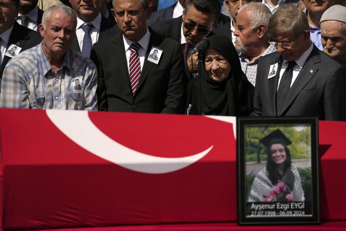 Several people stand behind a coffin with a photo of a woman resting against it.