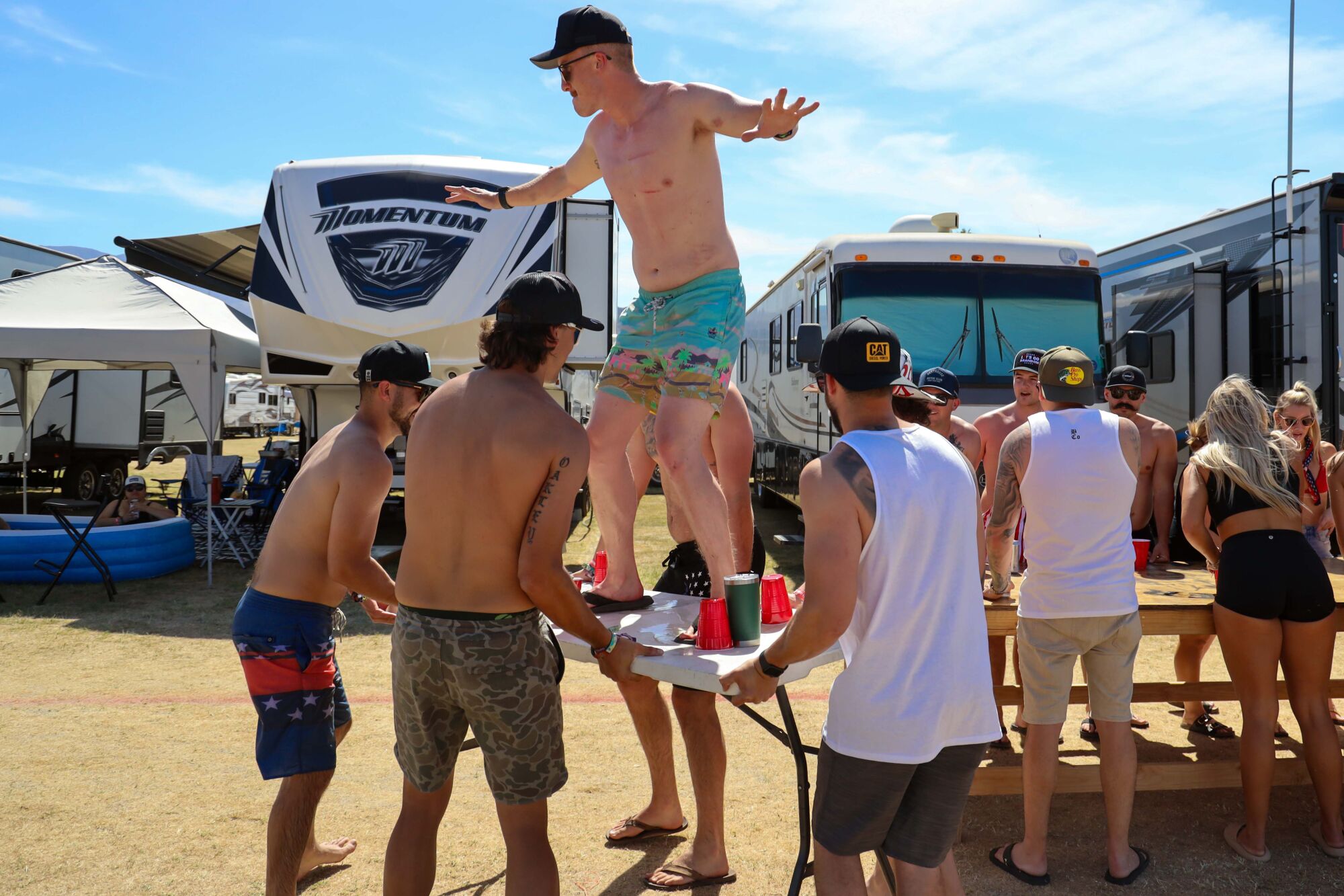 A country music fan strikes a surfer pose on a table as people play drinking games at the Stagecoach festival campgrounds.