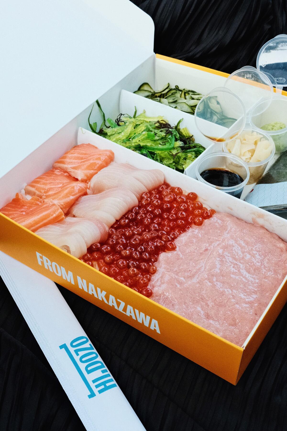 A takeout temaki kit on black background with toro, yellowtail, salmon, ikura, seaweed salad and nori in a Hi Dozo paper box.