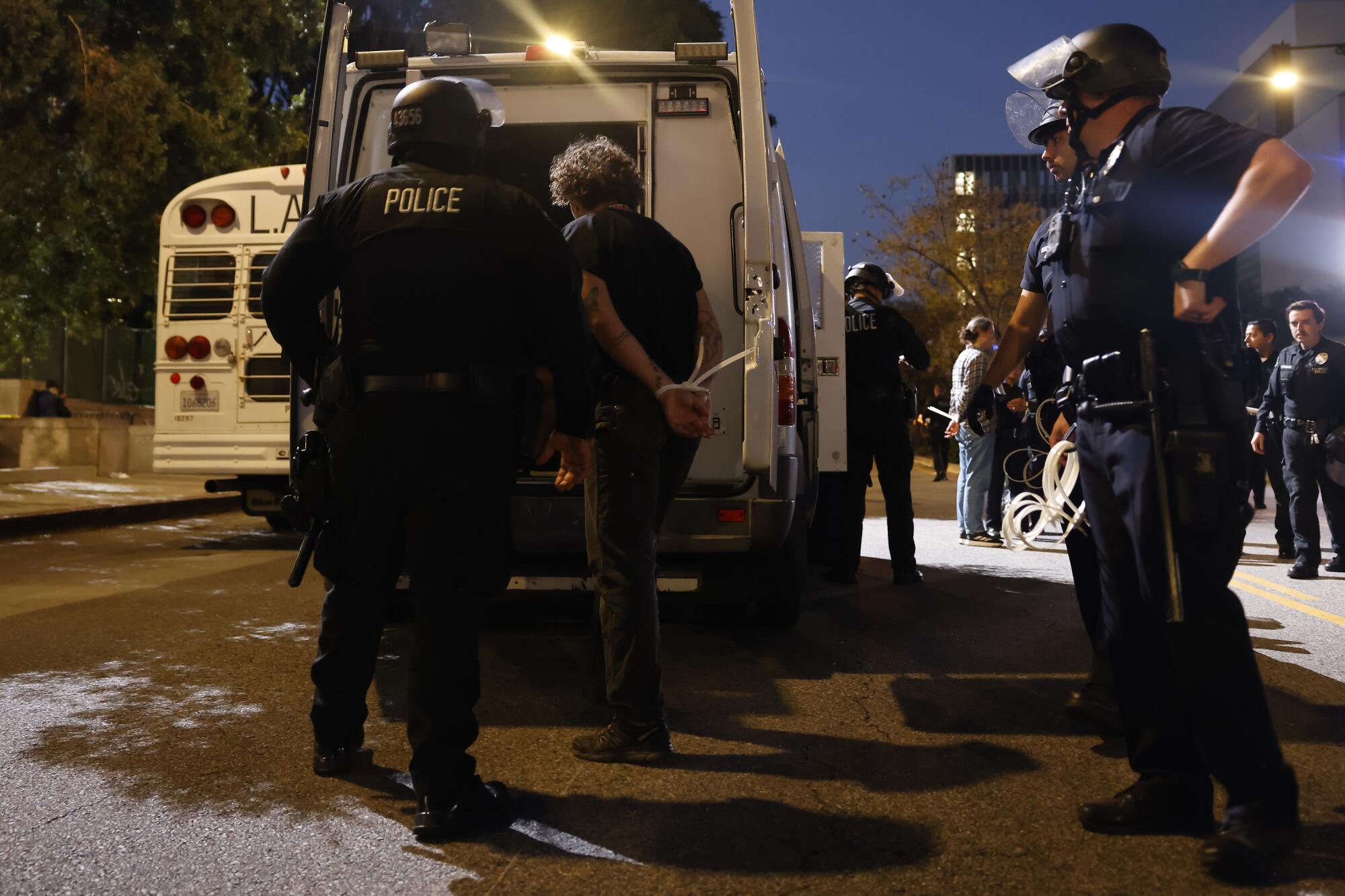 Helmeted police officers place a detainee in a van.