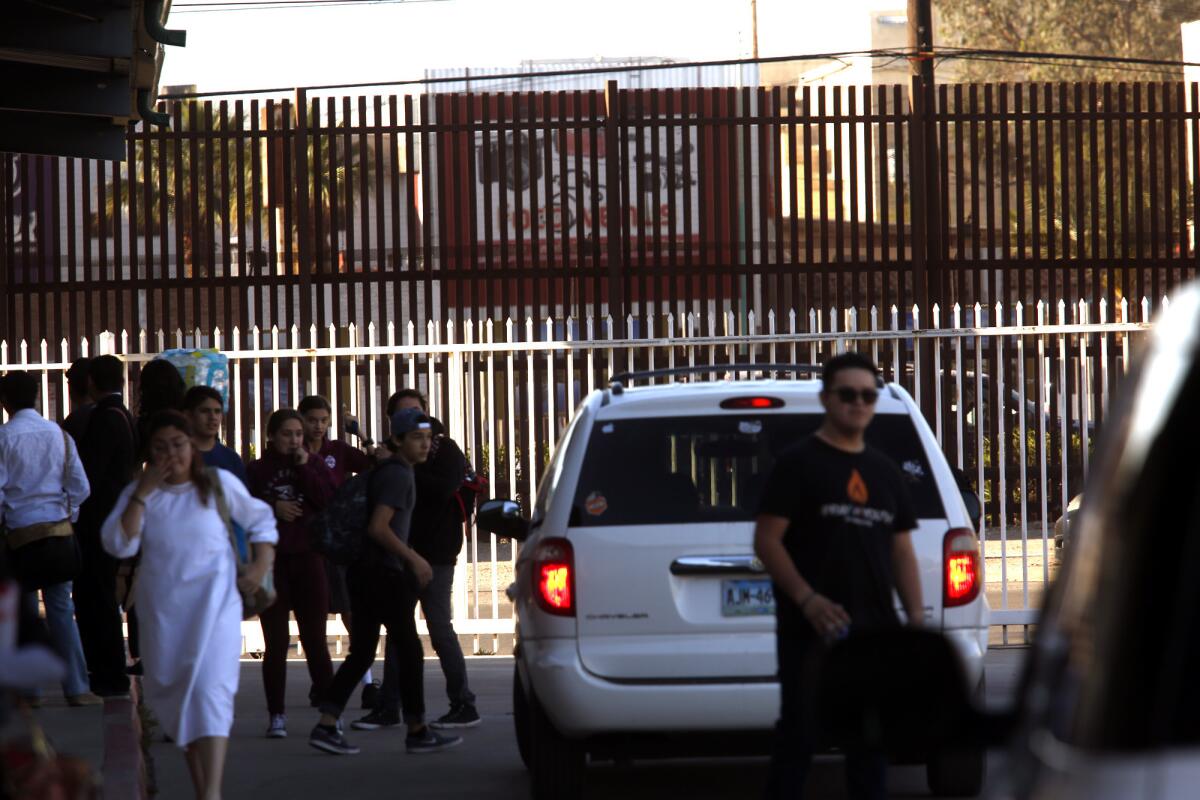 Students gather at the drop-off/pick-up spot for parents at the Calexico Mission School with the border fence, in brown, looming in the background in Calexico, Calif.