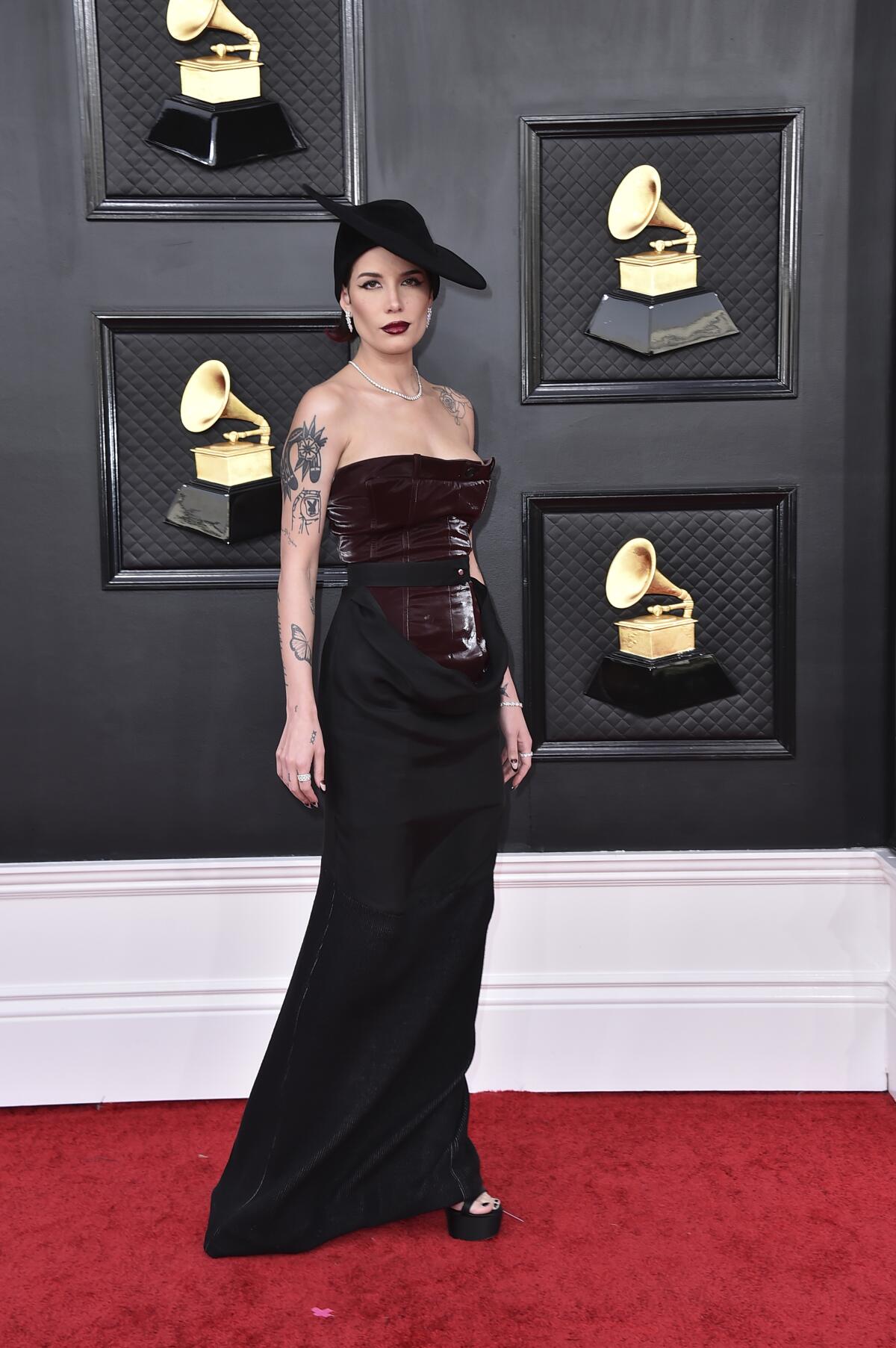 A female singer in a long black dress and a black hat walks the red carpet at the Grammys.