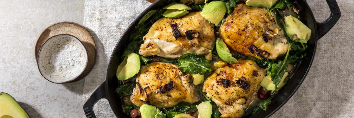 A pan of olive-brine baked chicken thighs nestled in a bed of kale and avocado 