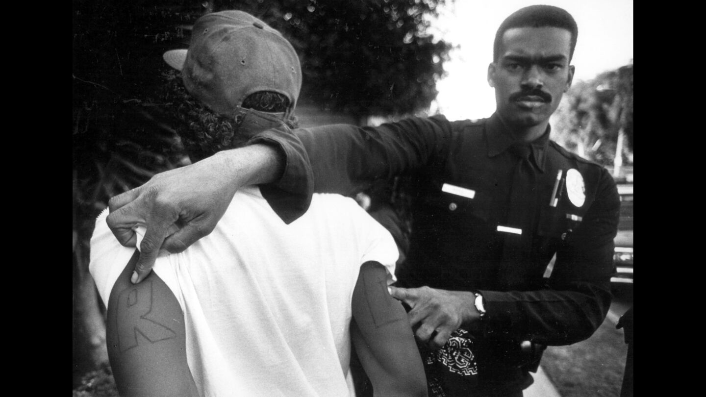 An LAPD officer shows the tattoo "RC," which stands for Raymond Street Crips, on a gang member.