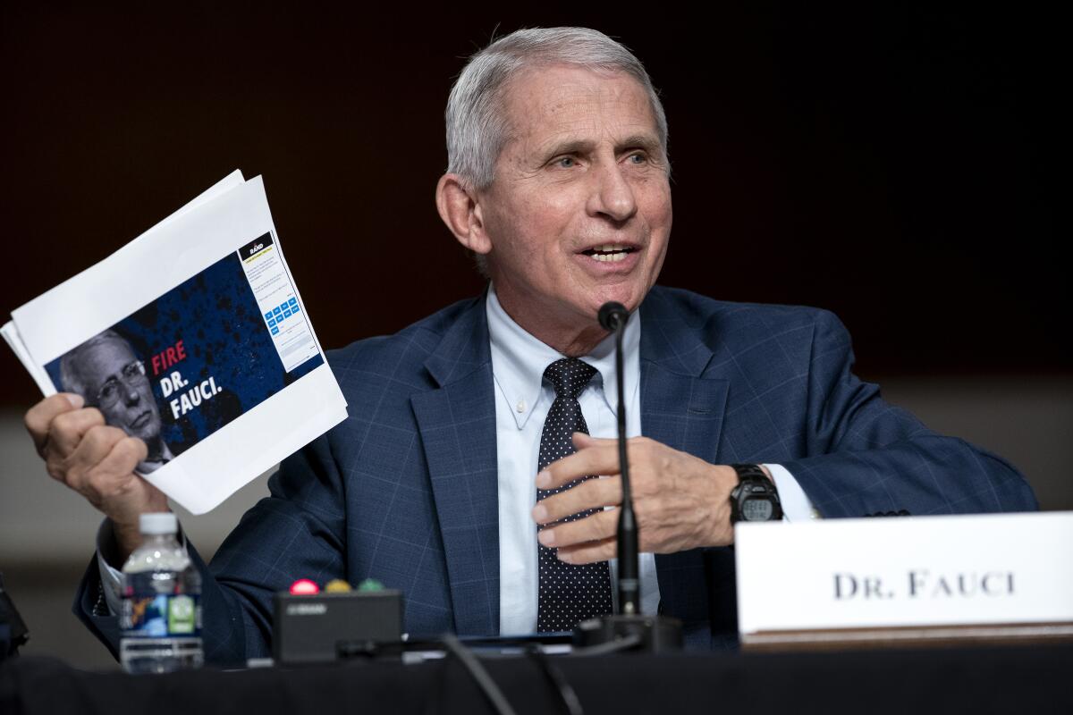 Dr. Anthony Fauci holds a paper while speaking into a microphone
