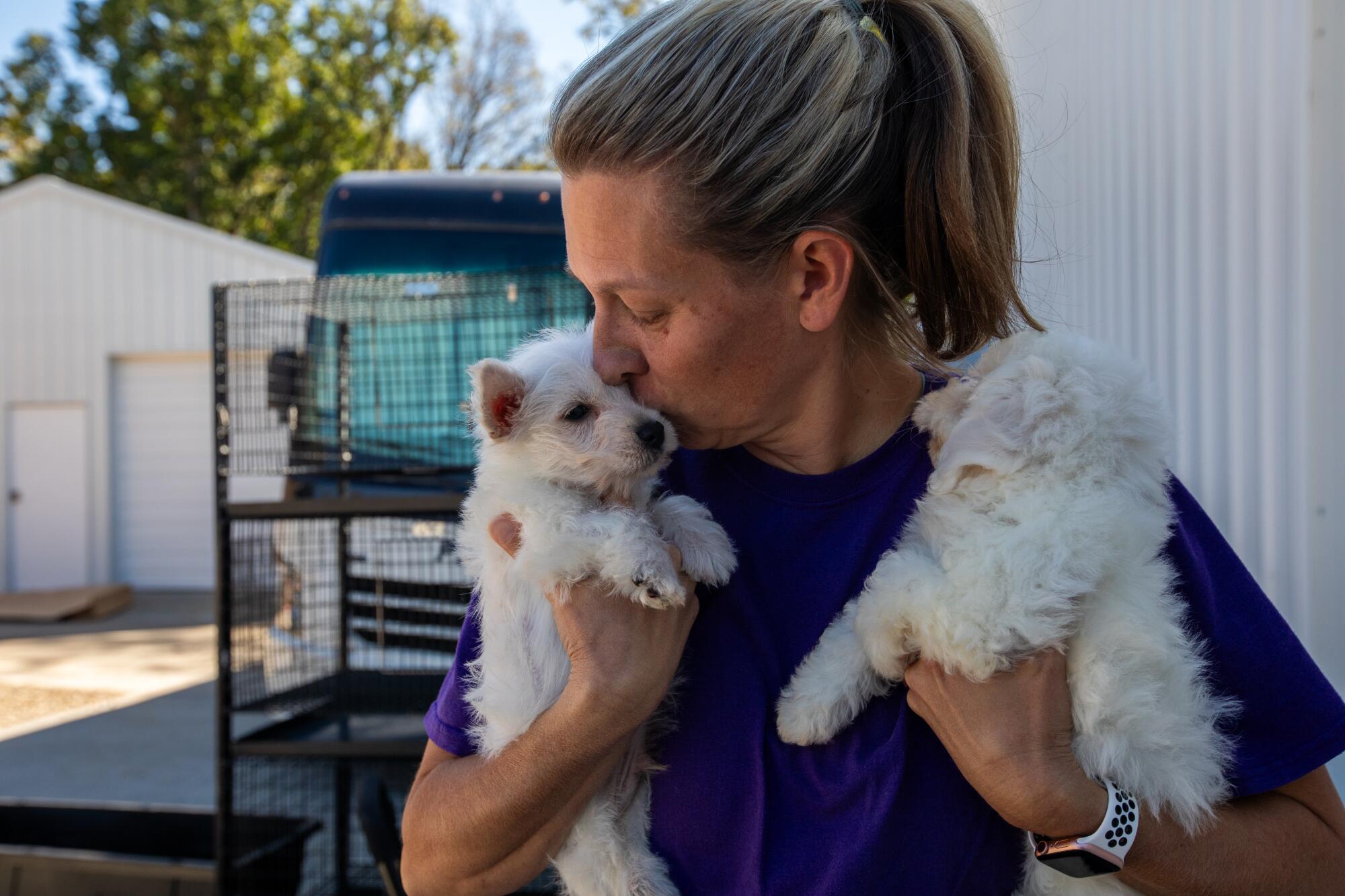 Tiffanie Kurz holding a puppy in each handing, kissing the one on her right