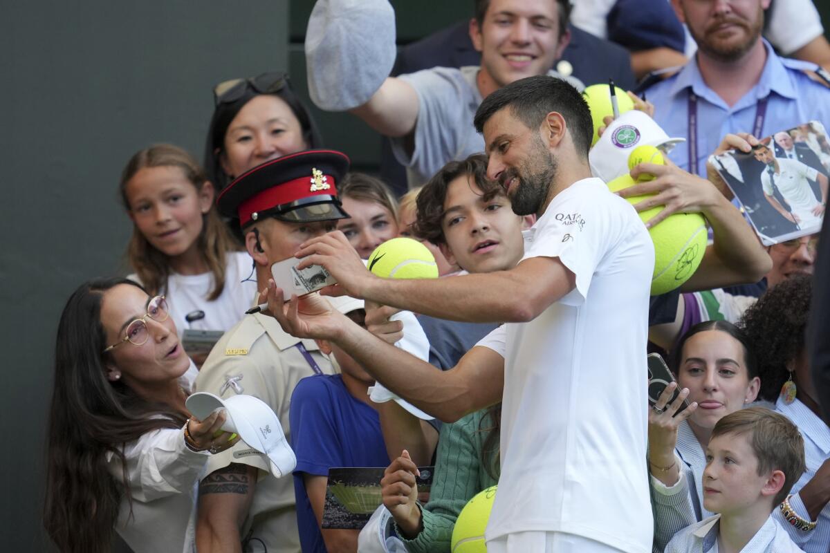 Novak Djokovic signs autographs and takes photos as he leaves the court after winning a Wimbledon quarterfinal match.
