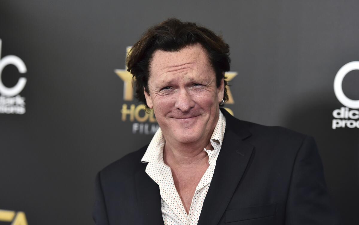 Michael Madsen smiles in a black blazer and white patterned shirt