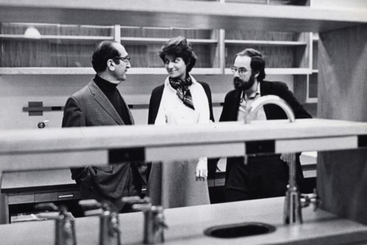 A woman and her two male colleagues stand in a lab.