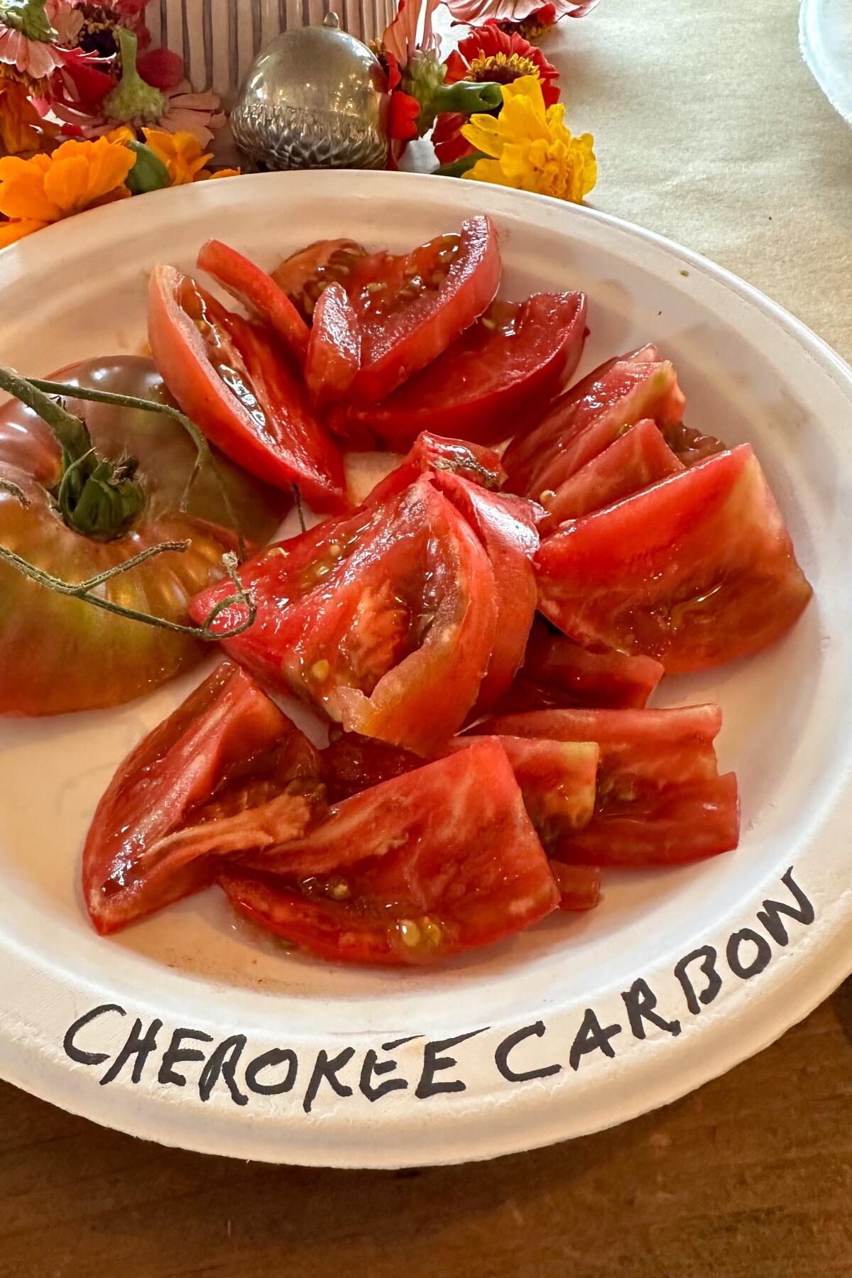 Red Cherokee Carbon tomatoes sliced on a labeled paper plate. 