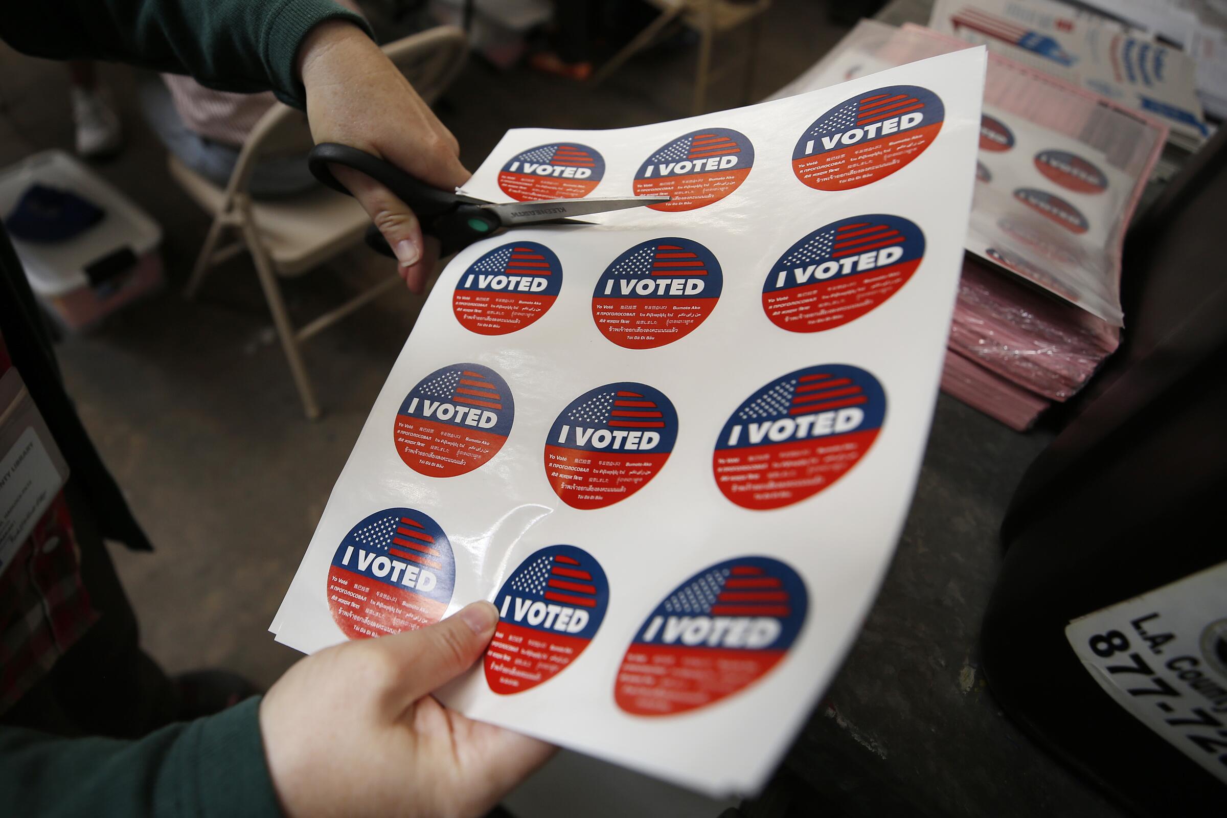 Scissors cut across a sheet of red, white and blue "I VOTED" stickers.