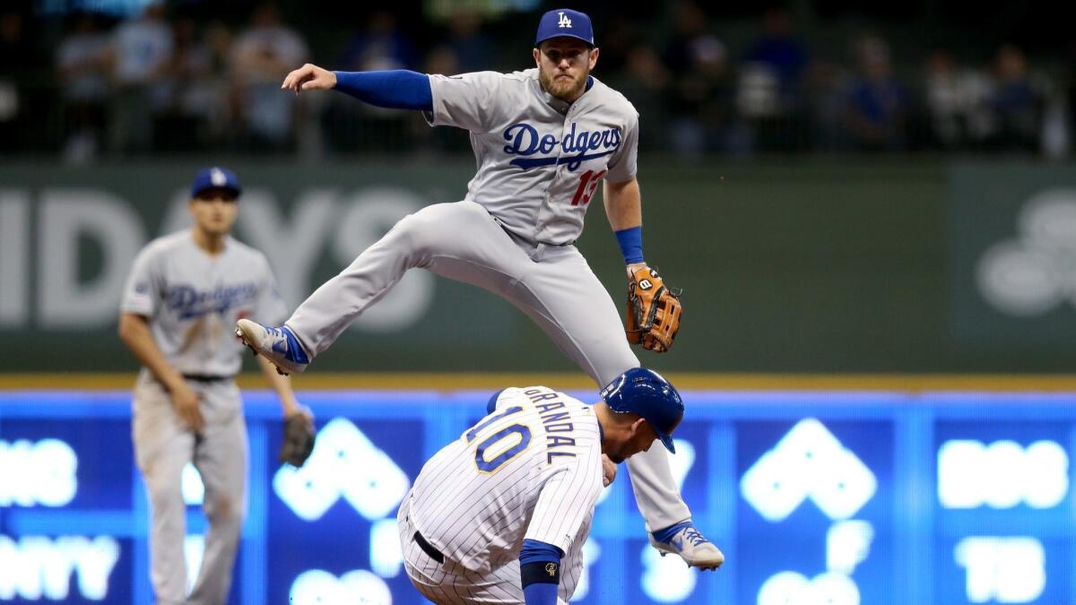 Max Muncy (13) of the Dodgers turns a double play past Yasmani Grandal (10) of the Brewers in the sixth inning of their game in Milwaukee.
