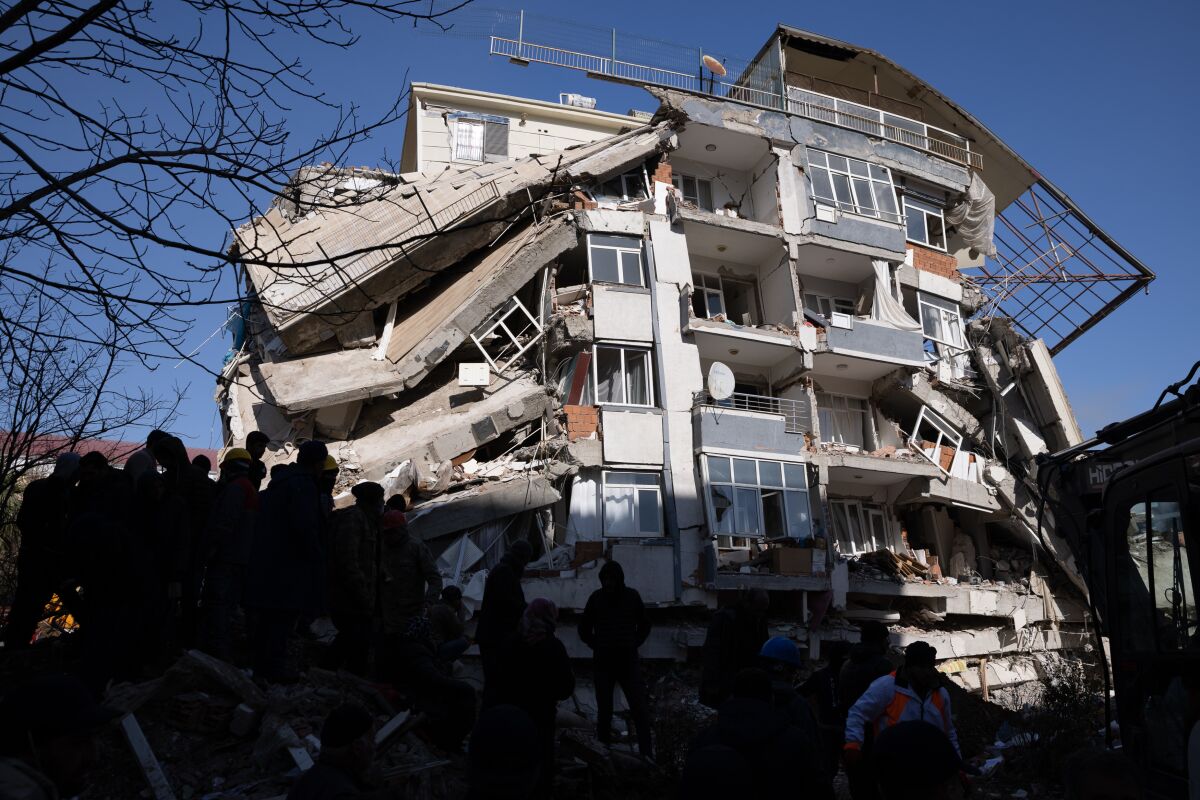People stand in the shadow of a badly damaged building