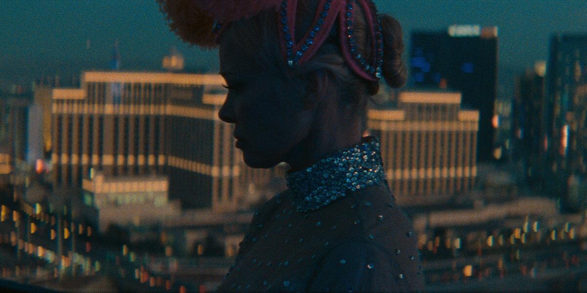 Pamela Anderson in a sparkly costume and headdress with a background image of a large hotel in "The Last Showgirl."