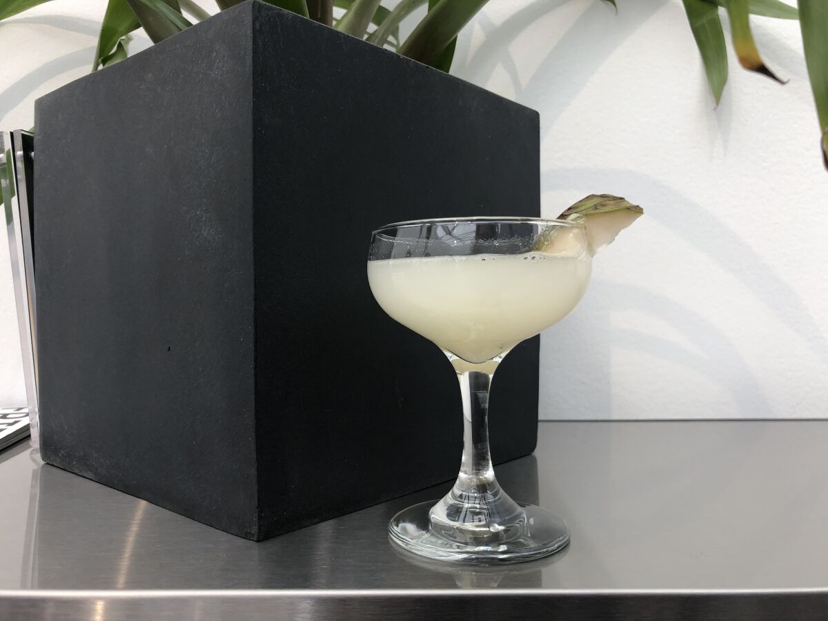 A photo of a cocktail with a piece of cherimoya fruit wedged on the rim.