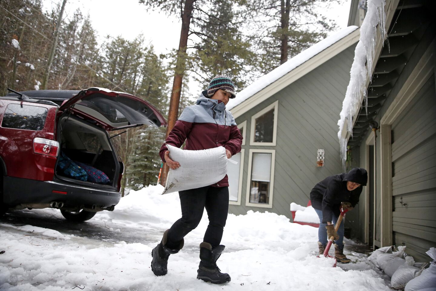 Monique Long hauls sandbags from her SUV to make a barrier to divert the rain and melting snow from flooding her garage, while her friend Jenna Shropshire, right, helps shovel snow, in Truckee, Calif.