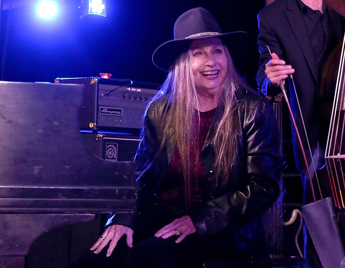 A female musician with long hair and wearing a cowboy hat, seated at a piano bench onstage