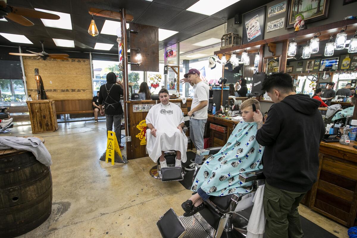Barbers cut hair at Hermanos Barbershop in Huntington Beach on Monday, two days after a burglary.