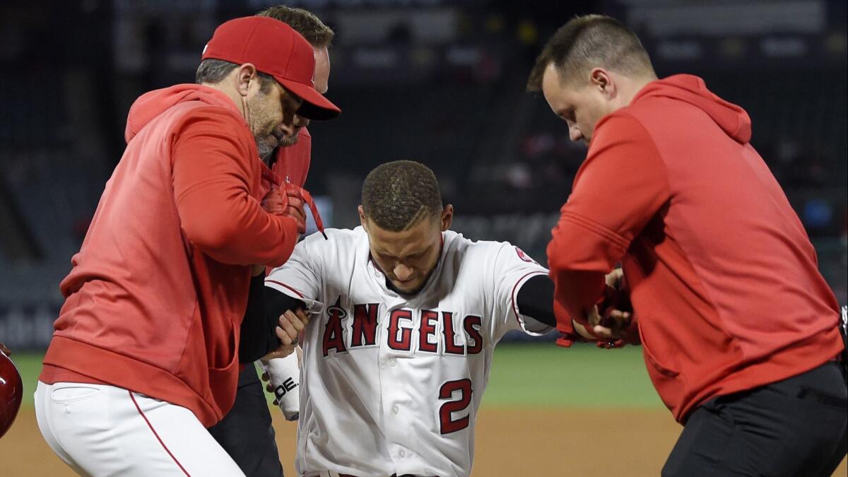 Angels' Andrelton Simmons is helped up by manager Brad Ausmus, left, and a trainer after he was injured while being thrown out at first during the eighth inning against the Minnesota Twins on Monday.