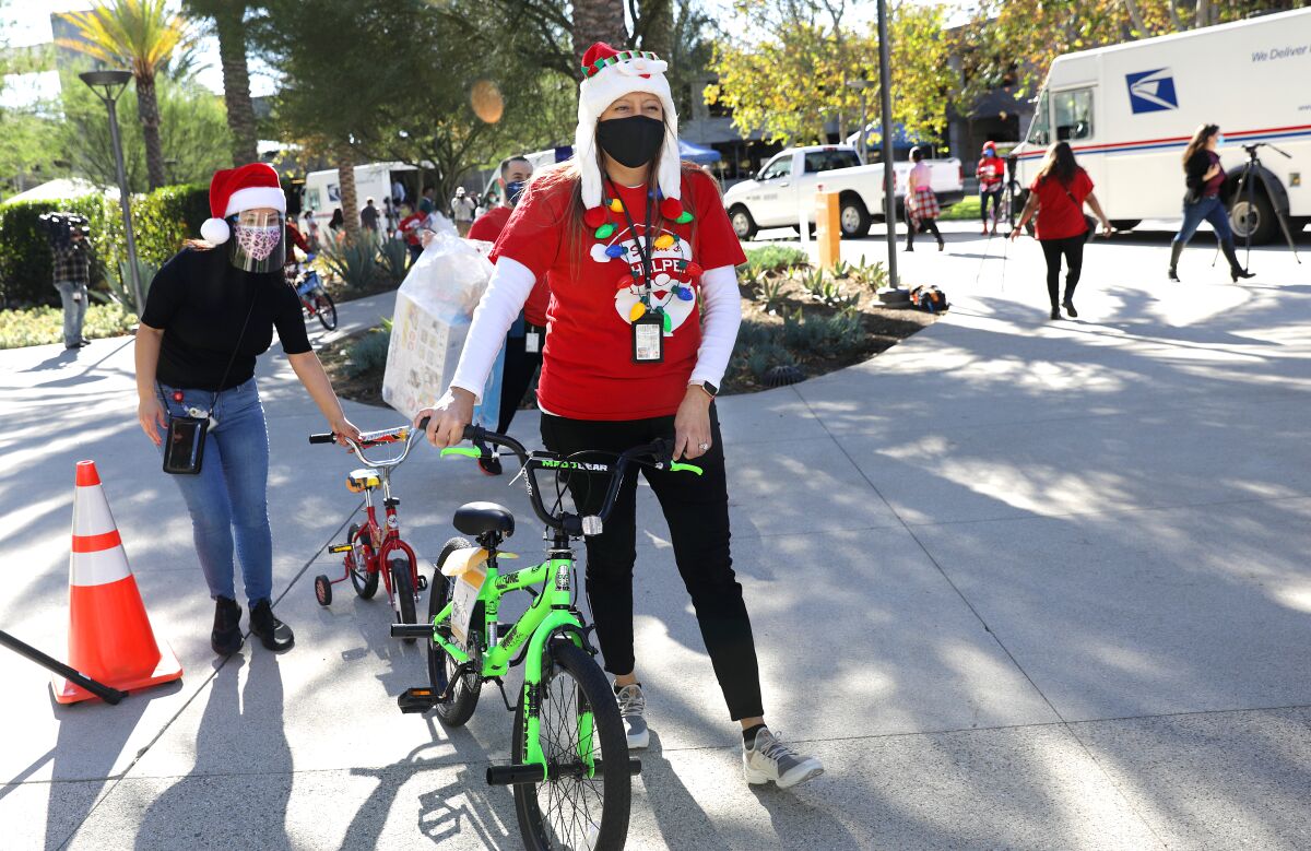 Two women dressed in holiday clothes walk children's bikes to a donation center. 